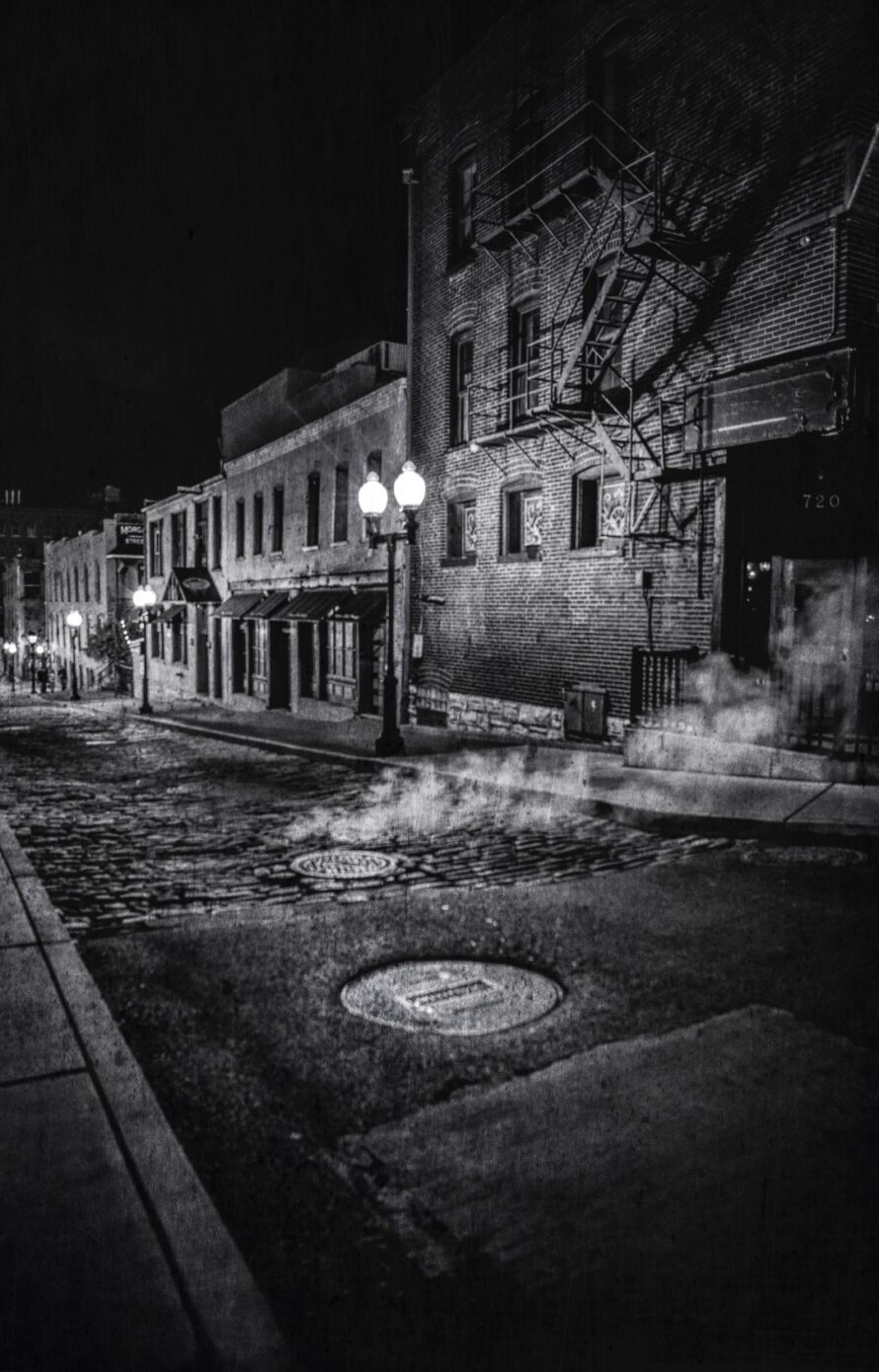 Steam escapes from a manhole along a street in Laclede&#039;s Landing at night.